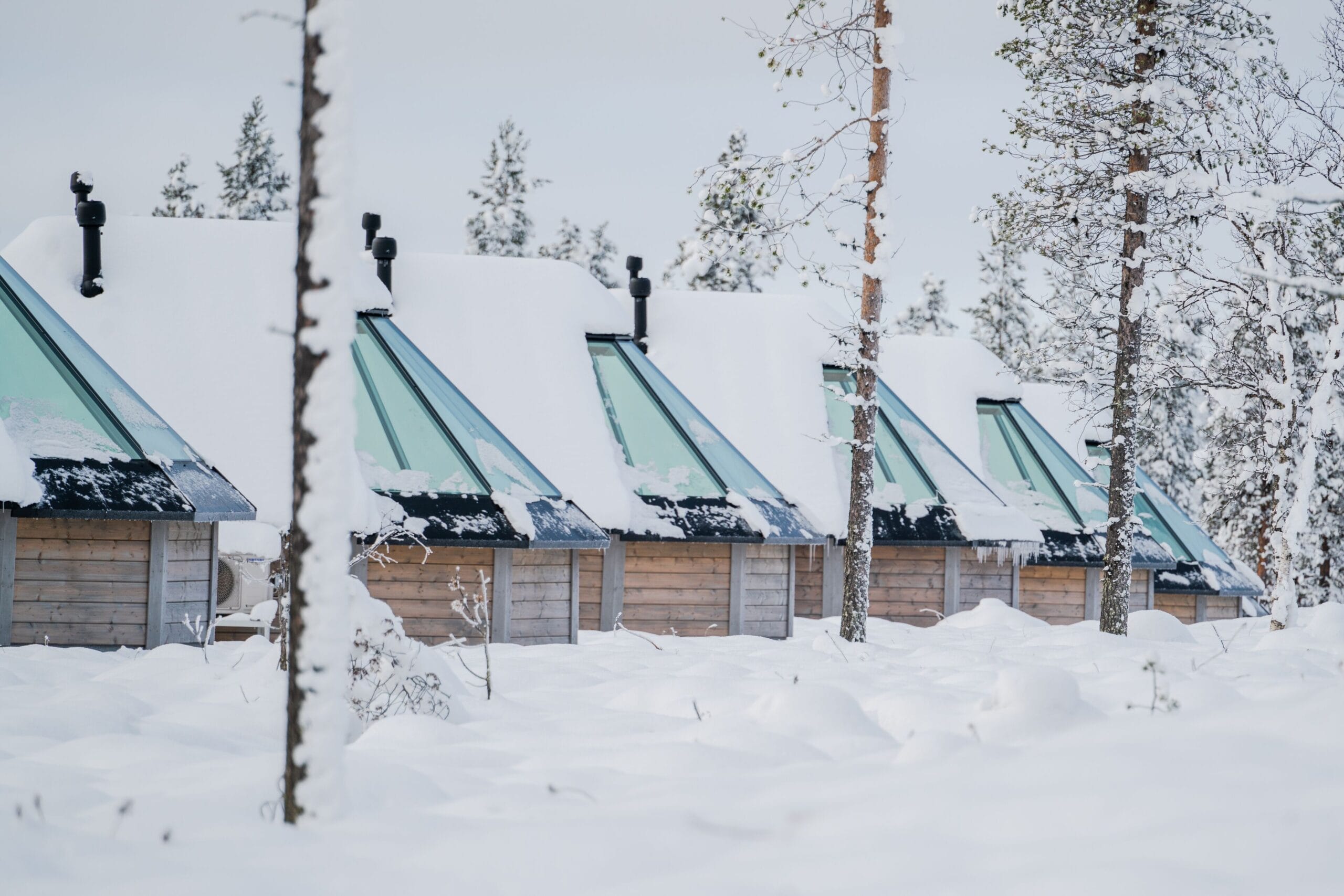 Glass-roof aurora cabin glowing in snowy pine forest at Northern Lights Village Saariselka, Finnish Lapland