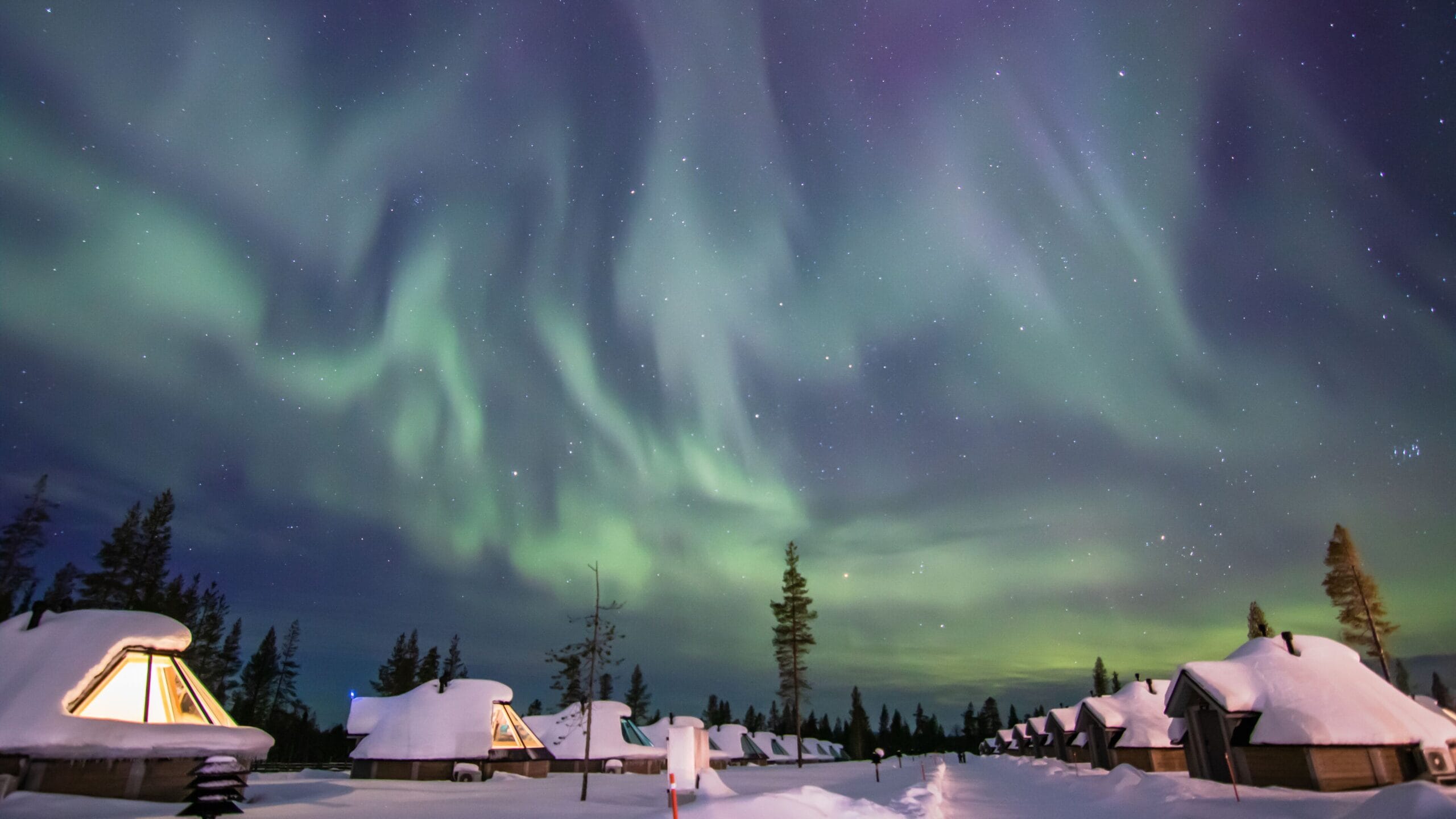 Row of glass-roof Aurora Cabins under the Northern Lights at Northern Lights Village Saariselka in far-north Finland