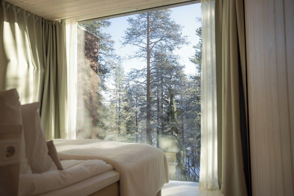 Treehouse suite interior with floor-to-ceiling window and Nordic design at Arctic TreeHouse Hotel, Lapland Finland