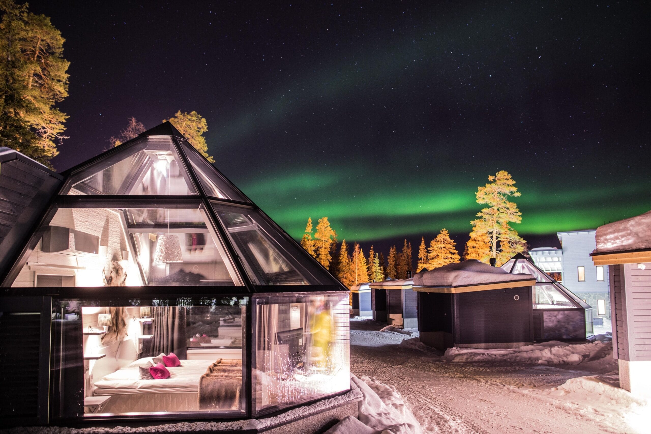 Glass igloo interior with bed under a heated glass ceiling at Santa's Hotel Aurora & Igloos, Luosto