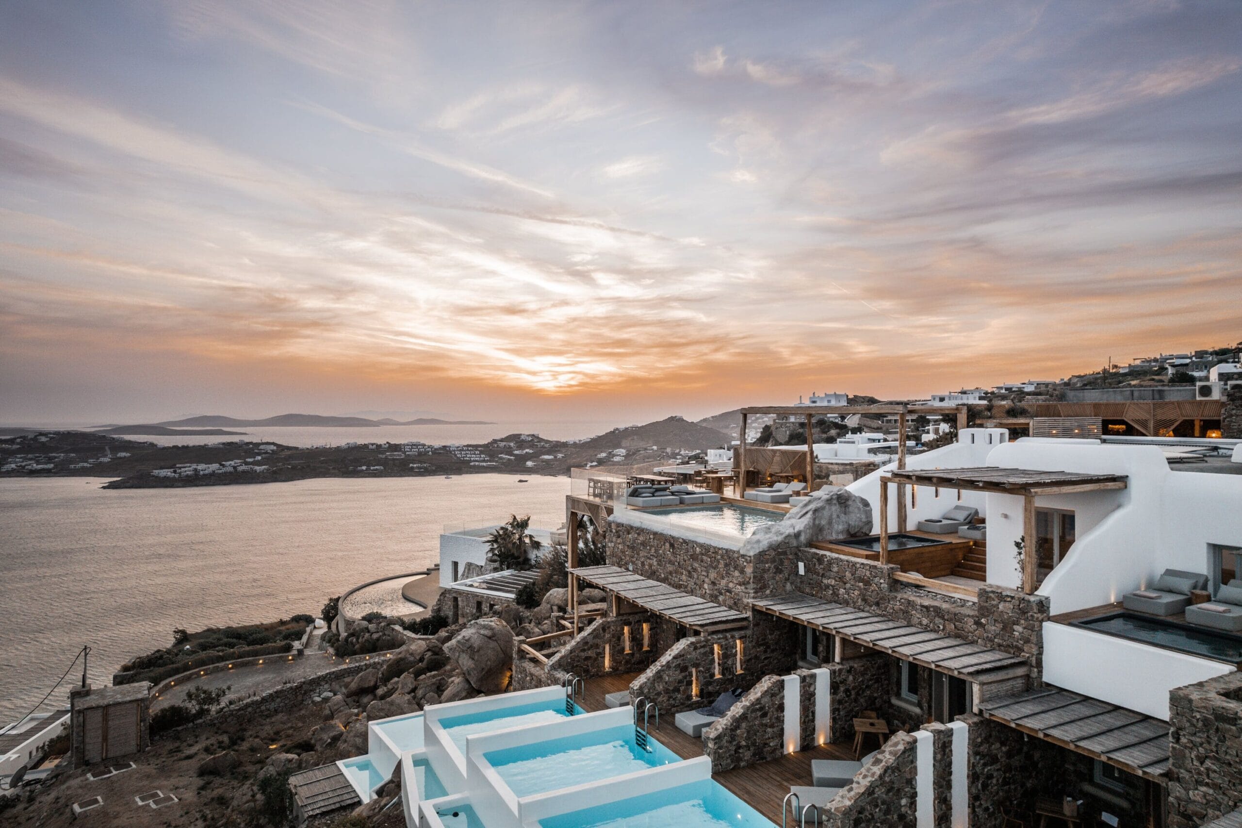 Private pool suites lit at sunset above Psarou Beach at Alissachni Mykonos